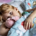 fetita bolnava in pat cu jucaria de plus